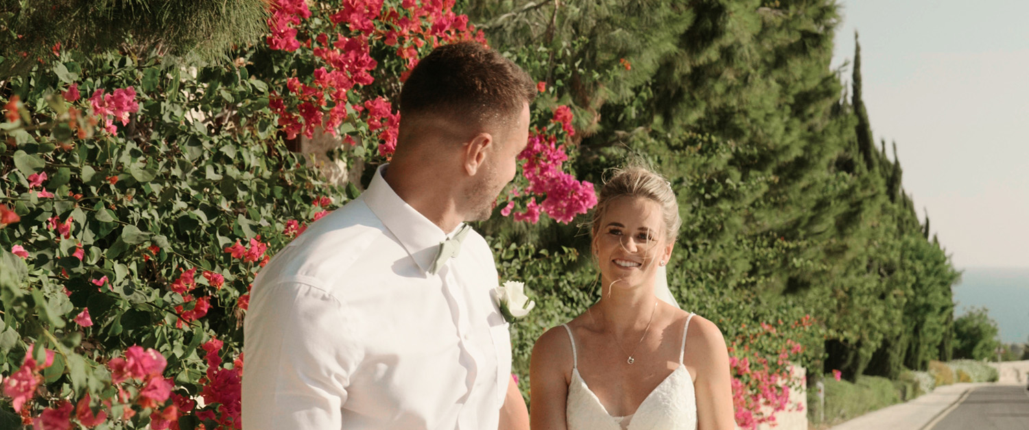 Ross and Suzi walking hand in hand along a vibrant, flower-lined path at Liopetro after their wedding ceremony, with smiles of joy and love.