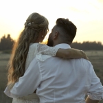Bride and groom hugging in a field at sunset with warm golden light in the background