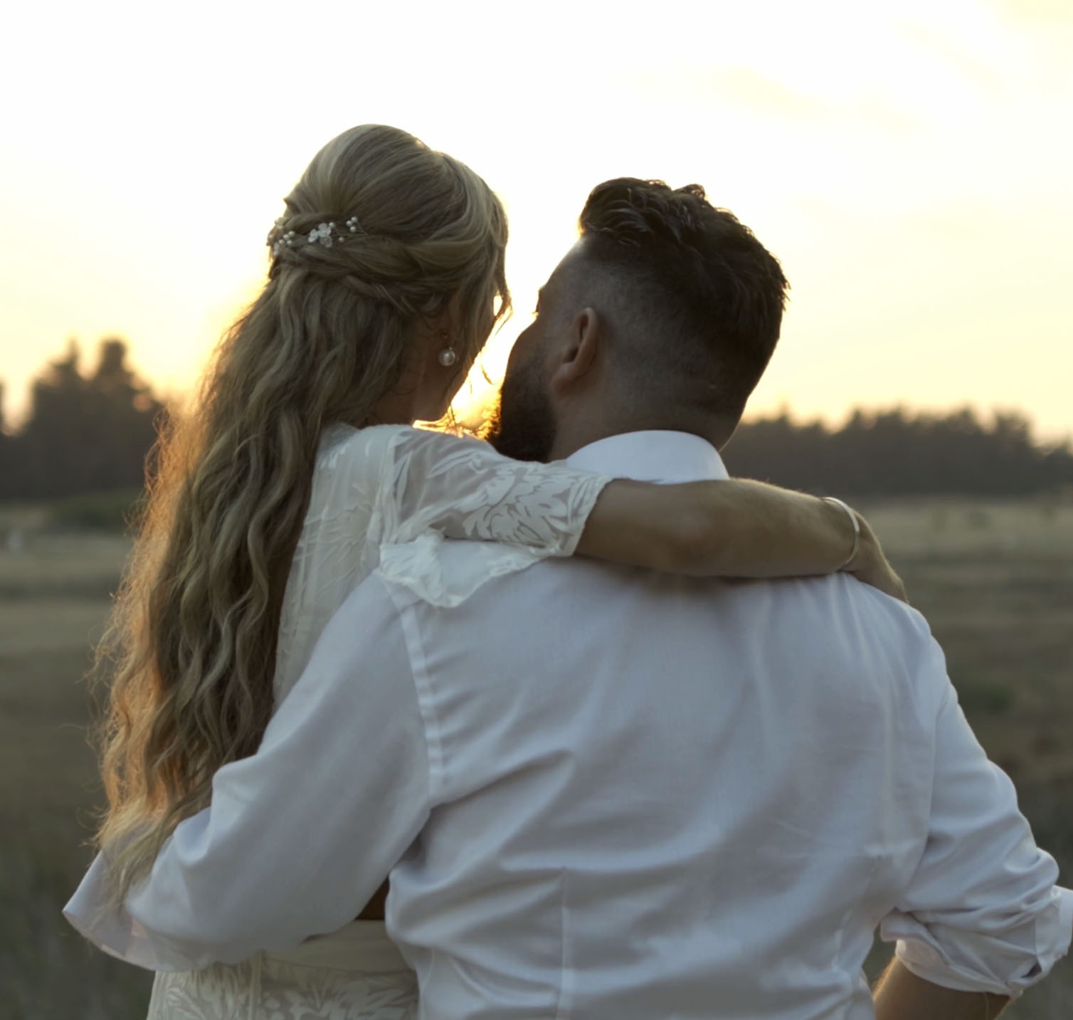 Bride and groom hugging in a field at sunset with warm golden light in the background
